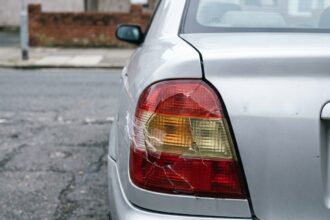 Feu arrière cassé sur une petite berline garée en ville, gros plan sur le plastique fissuré et jauni