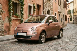 Fiat 500 rose gold garée sur des pavés dans un village européen, vue trois quarts avant avec reflets métalliques