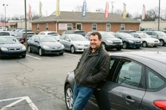 Homme souriant à côté d'une voiture d'occasion dans un concessionnaire