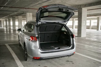 Coffre de la Peugeot 308 SW grand ouvert dans un parking urbain, vue trois quarts arrière montrant le volume de chargement et le revêtement en tissu